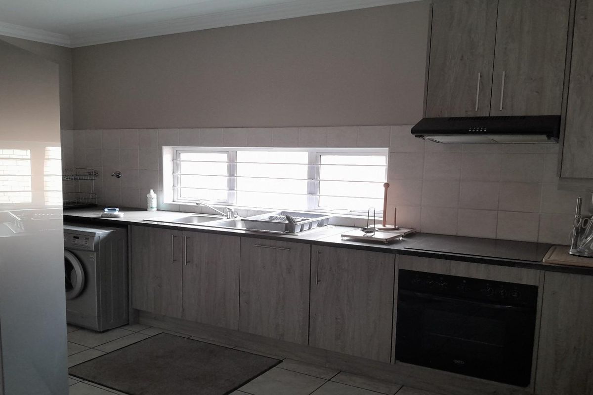 A functional kitchen featuring wood-look cabinetry, a built-in oven, extractor fan, and a stainless steel sink set against tiled splashbacks.