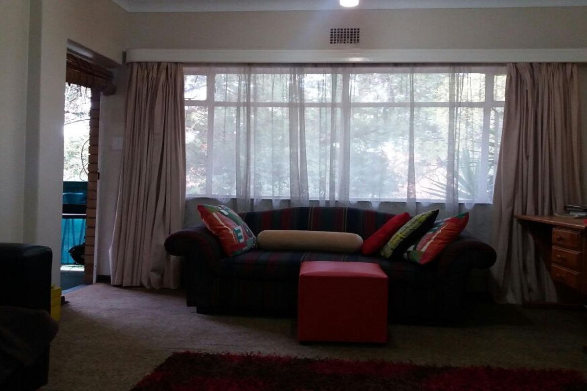 A living room featuring large windows with curtain tracks, carpeted flooring, and access to an outdoor patio area.