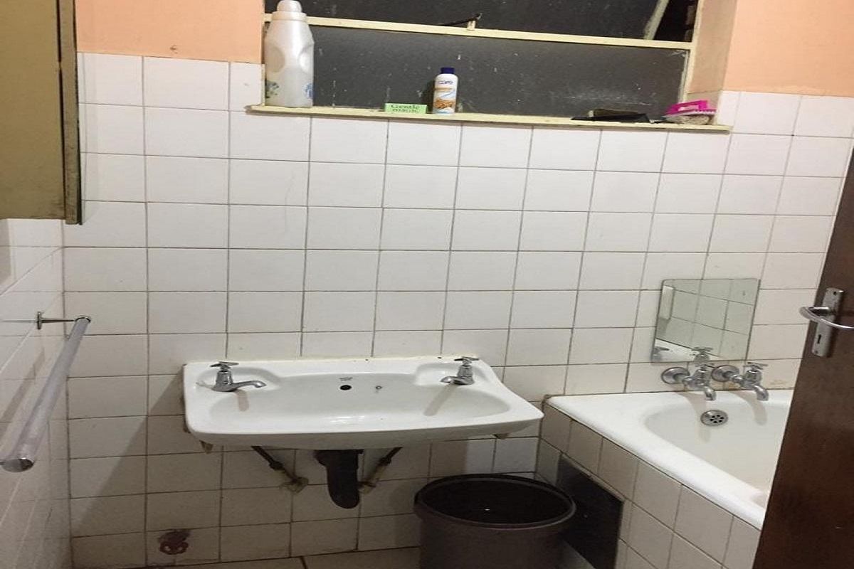A dated bathroom featuring a wall-mounted basin, bathtub, and tiled walls, requiring cosmetic updates and maintenance to improve its overall condition.