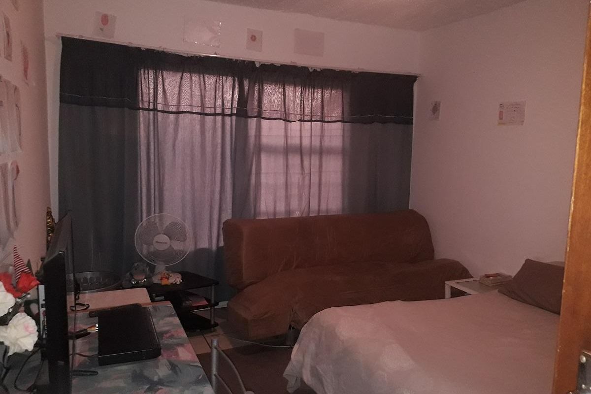 A bedroom featuring tiled flooring and a large window with curtains, providing a functional living space.