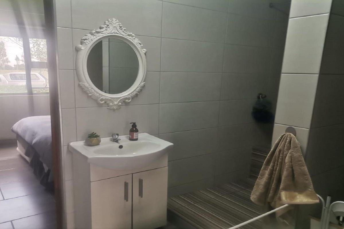A functional bathroom featuring a vanity basin, tiled walls, and a walk-in shower area, with an adjacent view into a bedroom.