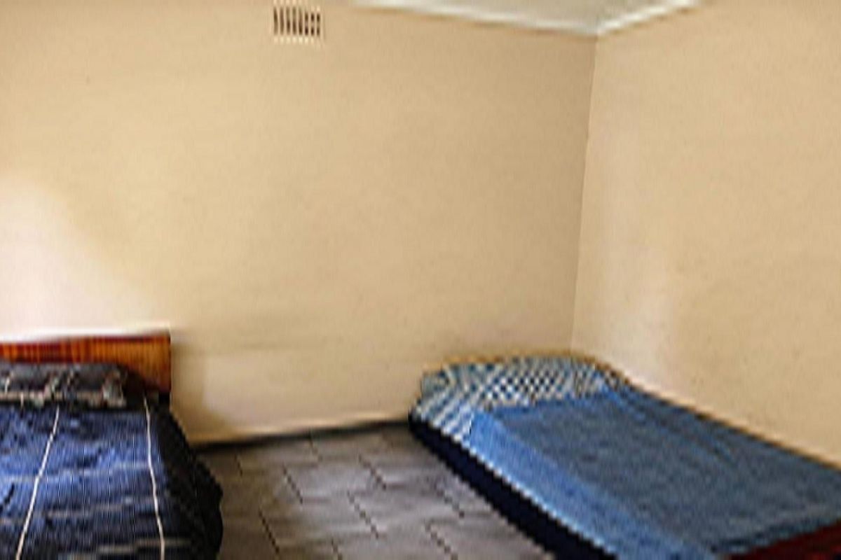 A simple bedroom space featuring plain walls and tiled flooring, providing a functional area for sleeping arrangements.