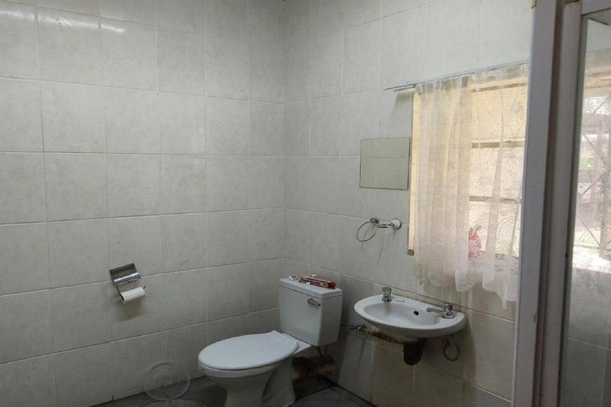A functional bathroom featuring full-height wall tiling, a standard toilet, and a wall-mounted basin with exposed plumbing.