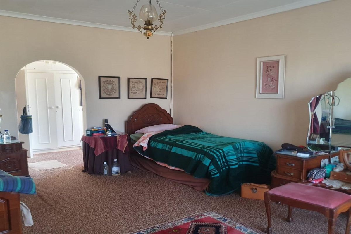A spacious bedroom featuring carpeted flooring, a classic arched doorway leading to an adjacent room, and traditional ceiling lighting.