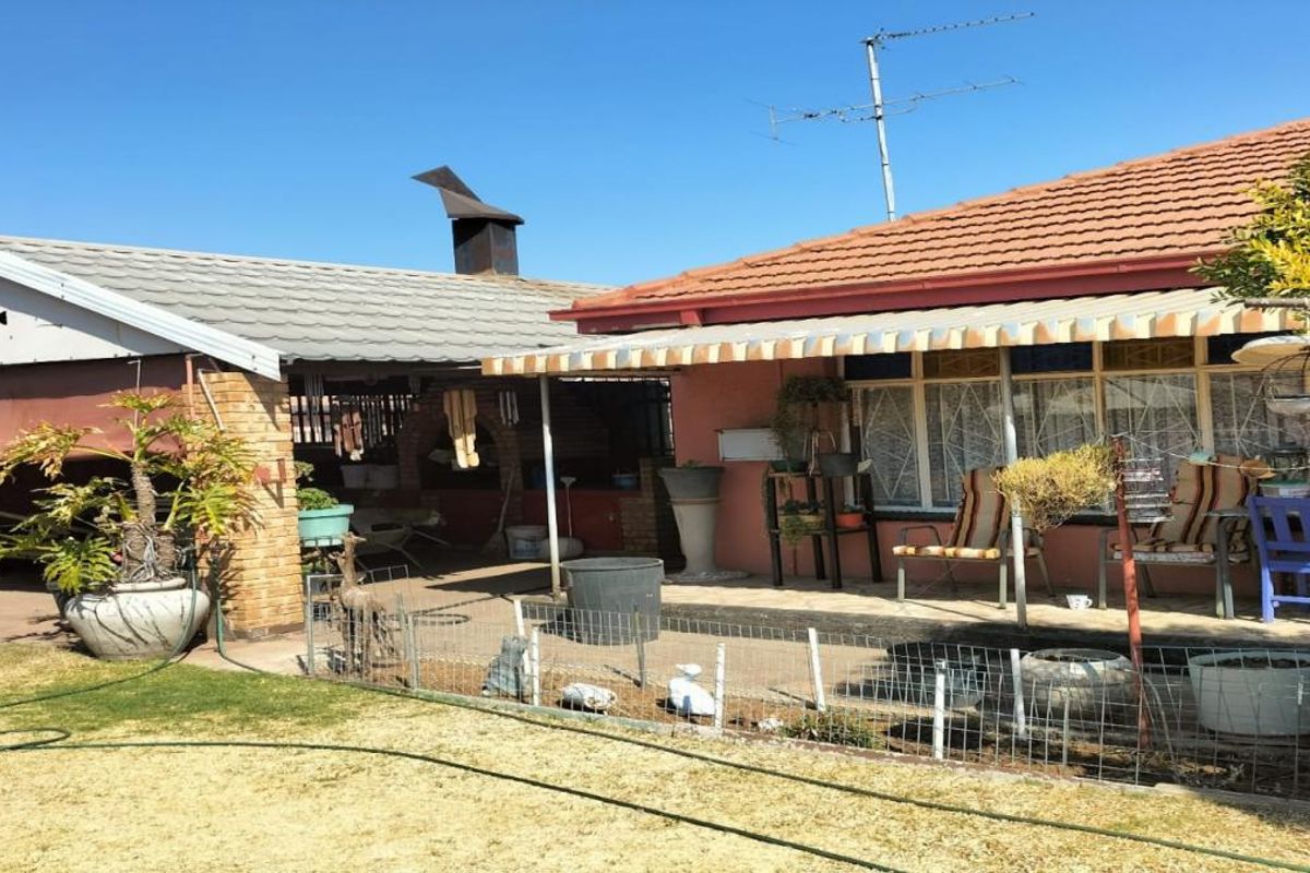 Rear exterior view featuring a covered patio area, brick chimney, and tiled roof structure overlooking a garden space.