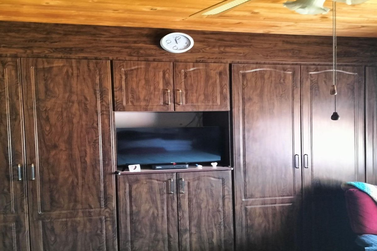 A bedroom featuring extensive built-in dark wood-grain cabinetry with integrated shelving and a timber-paneled ceiling.
