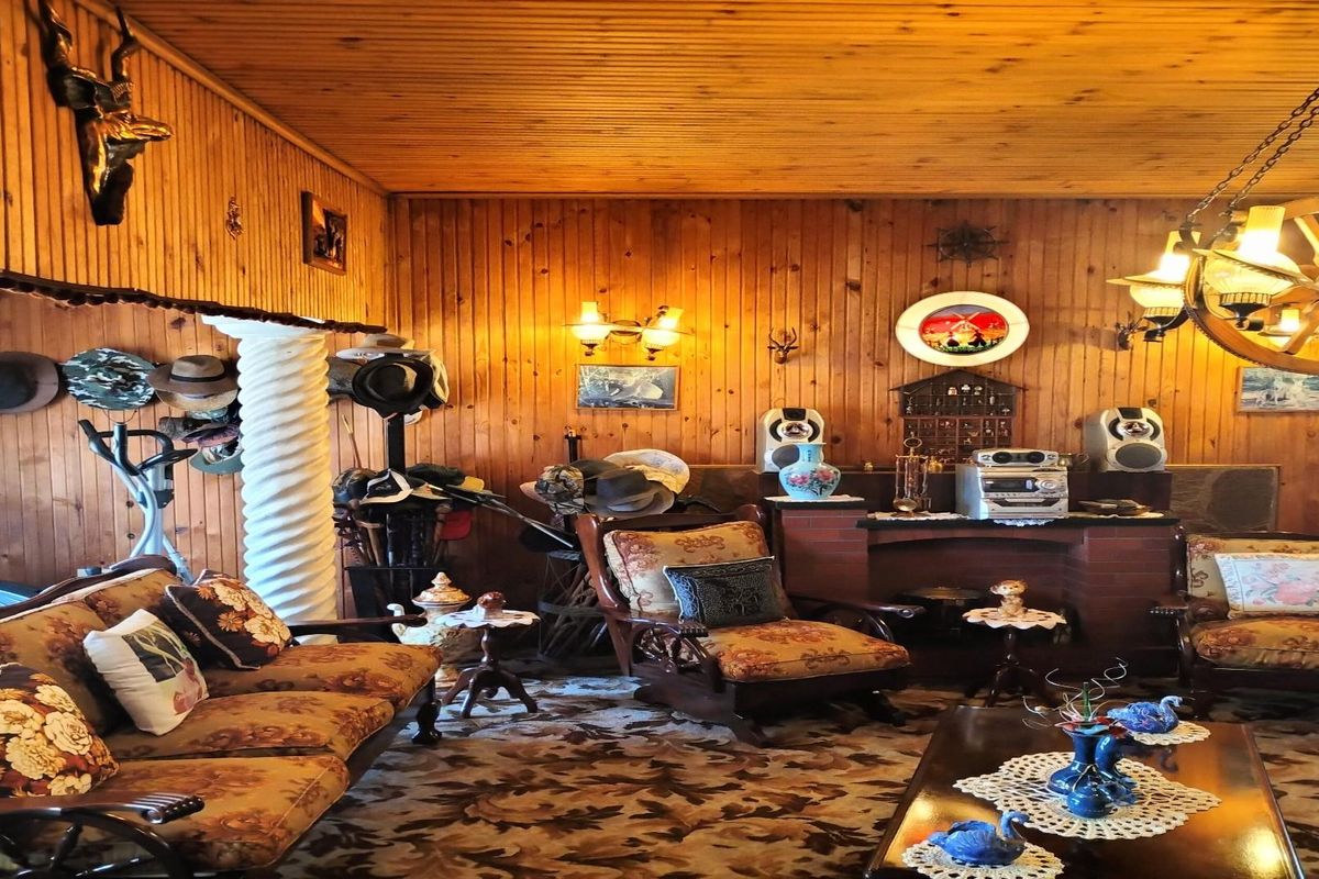 A rustic living room featuring extensive wood-paneled walls, a brick fireplace surround, and a decorative wagon wheel chandelier.