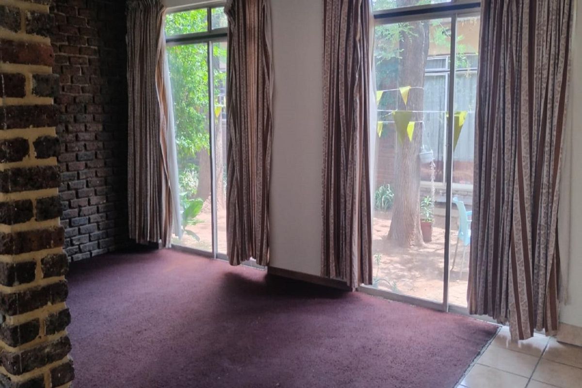 Living room featuring a prominent exposed brick feature wall, carpeted flooring, and large sliding glass doors providing direct access to the garden.