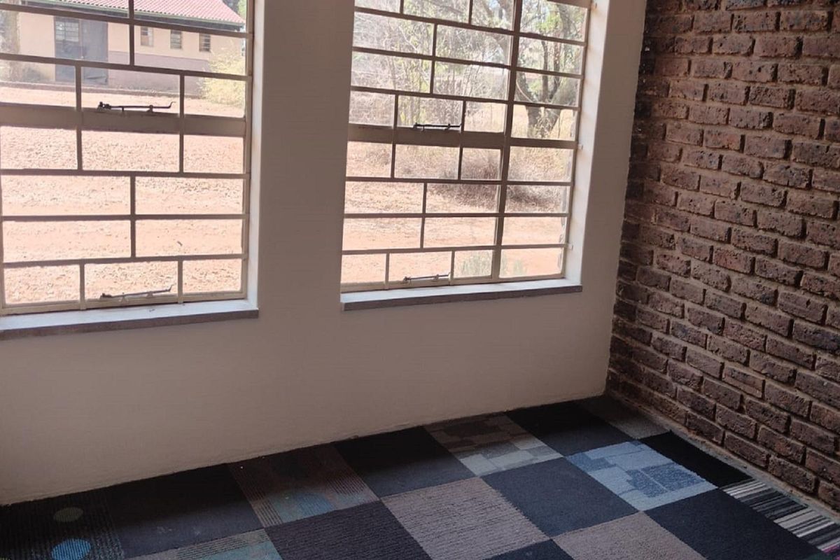 A bedroom featuring exposed brick wall detailing, carpet tile flooring, and security bars on the windows overlooking the farm grounds.