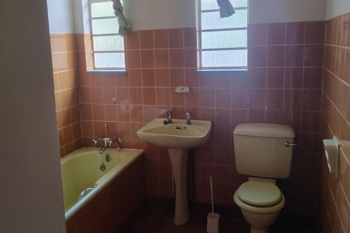 A dated bathroom featuring original colored sanitaryware, a bathtub, pedestal basin, and floor-to-ceiling wall tiles.