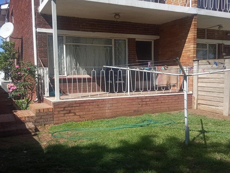 Rear view of the apartment featuring a covered patio, brick facade, and a private garden area with boundary walling.