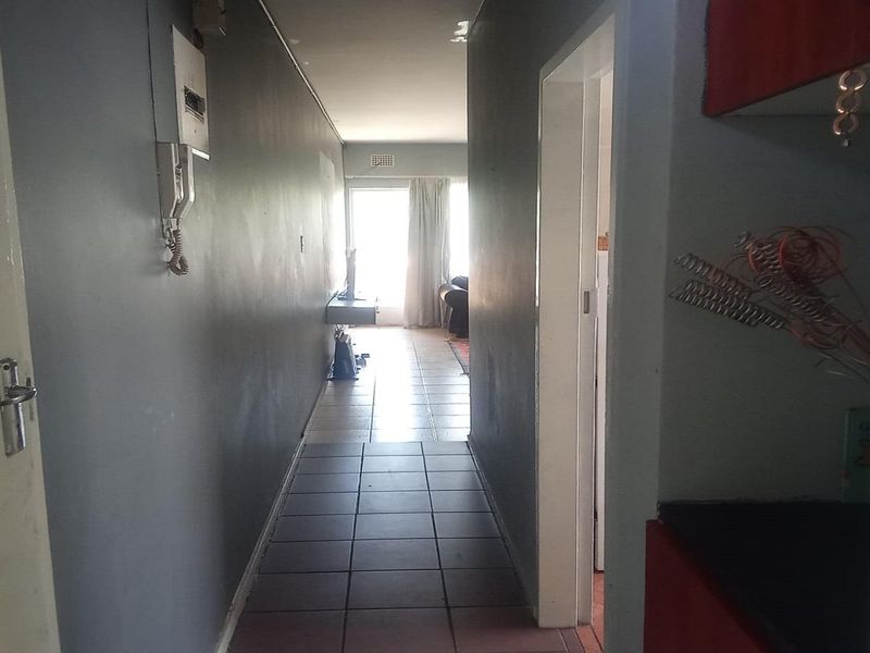 A narrow hallway with tiled flooring leading towards an open-plan living area, featuring an intercom system and neutral wall finishes.