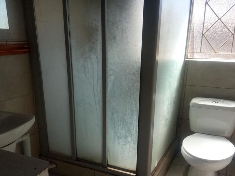 A functional bathroom featuring a shower enclosure, pedestal basin, and toilet, with tiled finishes and natural light from an obscured glass window.