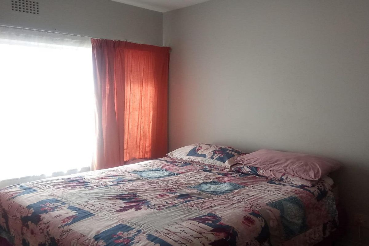 A standard bedroom featuring a large window with natural light and a built-in ventilation grille.