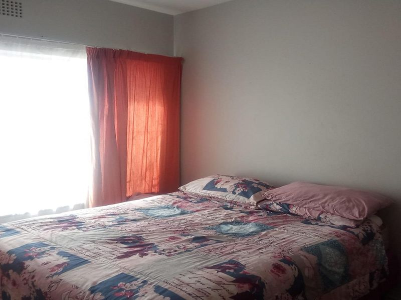 A standard bedroom featuring a large window with natural light and a built-in ventilation grille.