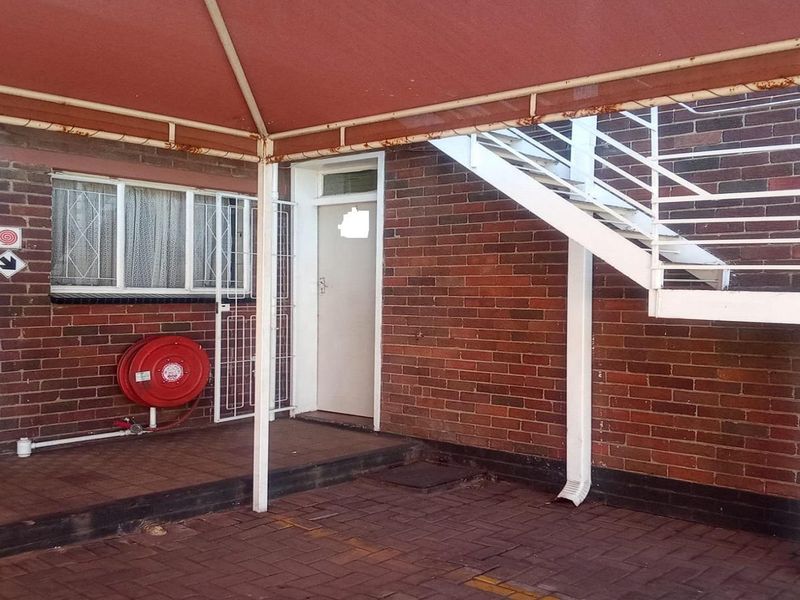 Rear exterior area featuring a paved patio, brick facade, metal staircase, and a fixed awning with some visible surface rust.