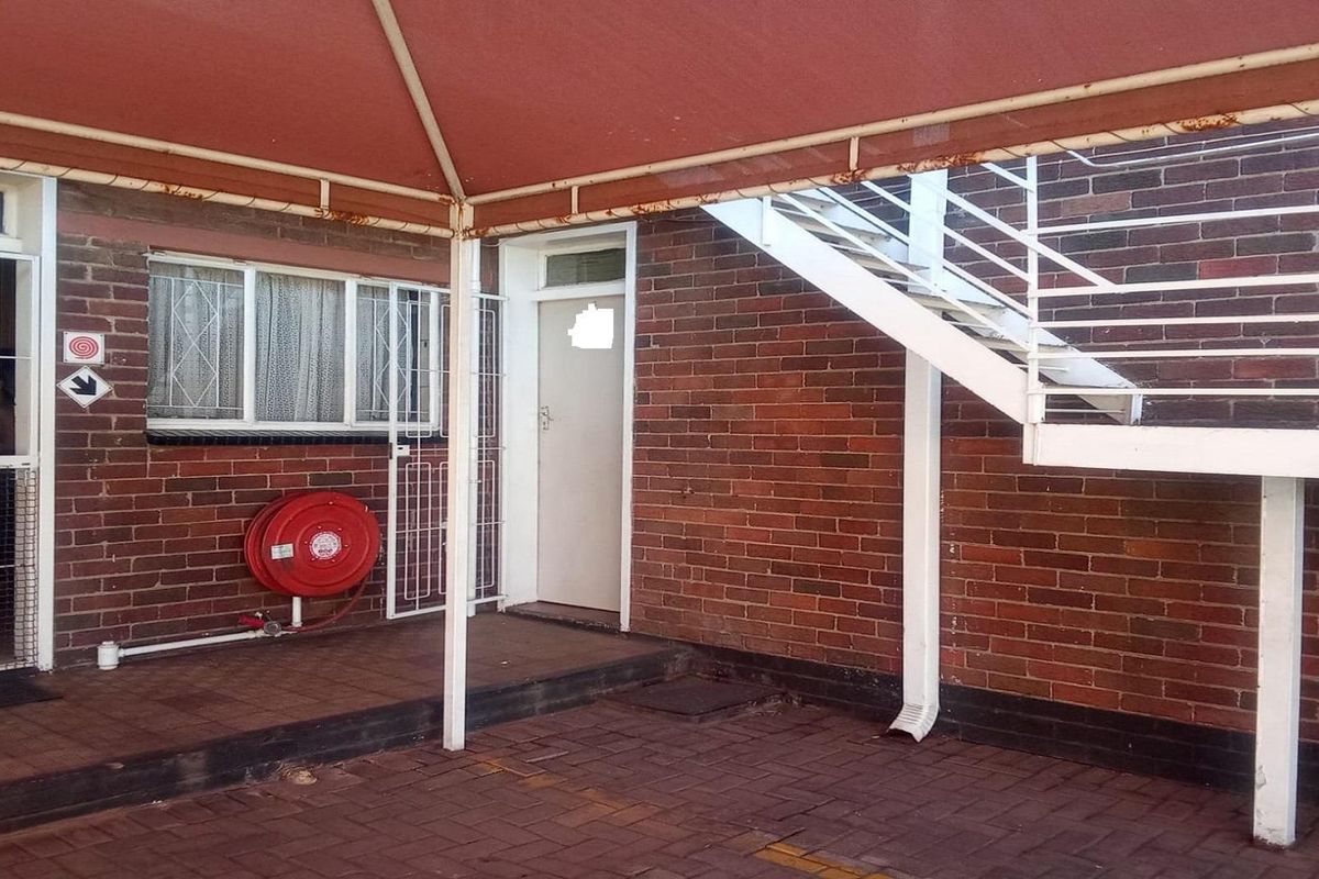 Rear exterior area featuring a paved patio, brick facade, metal staircase, and a fixed awning with some visible surface rust.