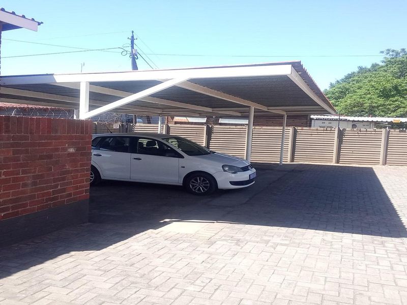 A paved outdoor parking area featuring a covered carport structure and secure perimeter walling.