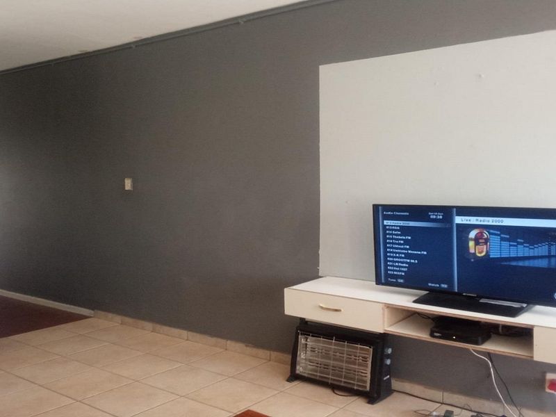 A living room area featuring ceramic floor tiles and a two-tone painted wall, showing signs of wear near the ceiling.