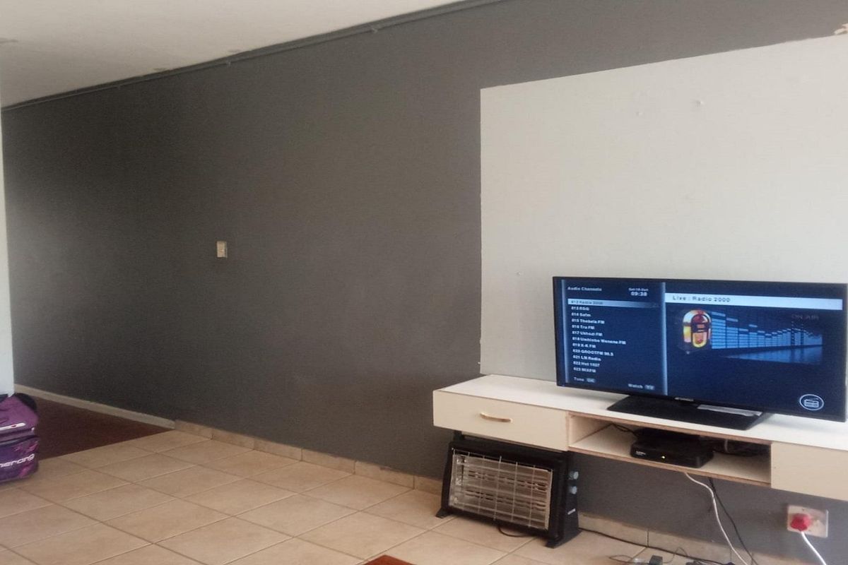 A living room area featuring ceramic floor tiles and a two-tone painted wall, showing signs of wear near the ceiling.