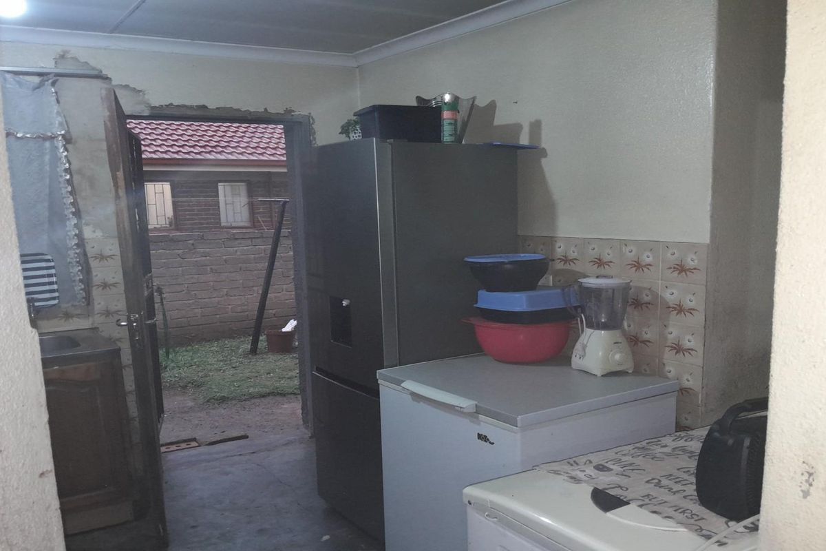 A kitchen area showing signs of wear, featuring tiled splashbacks and direct access to the rear exterior of the property.