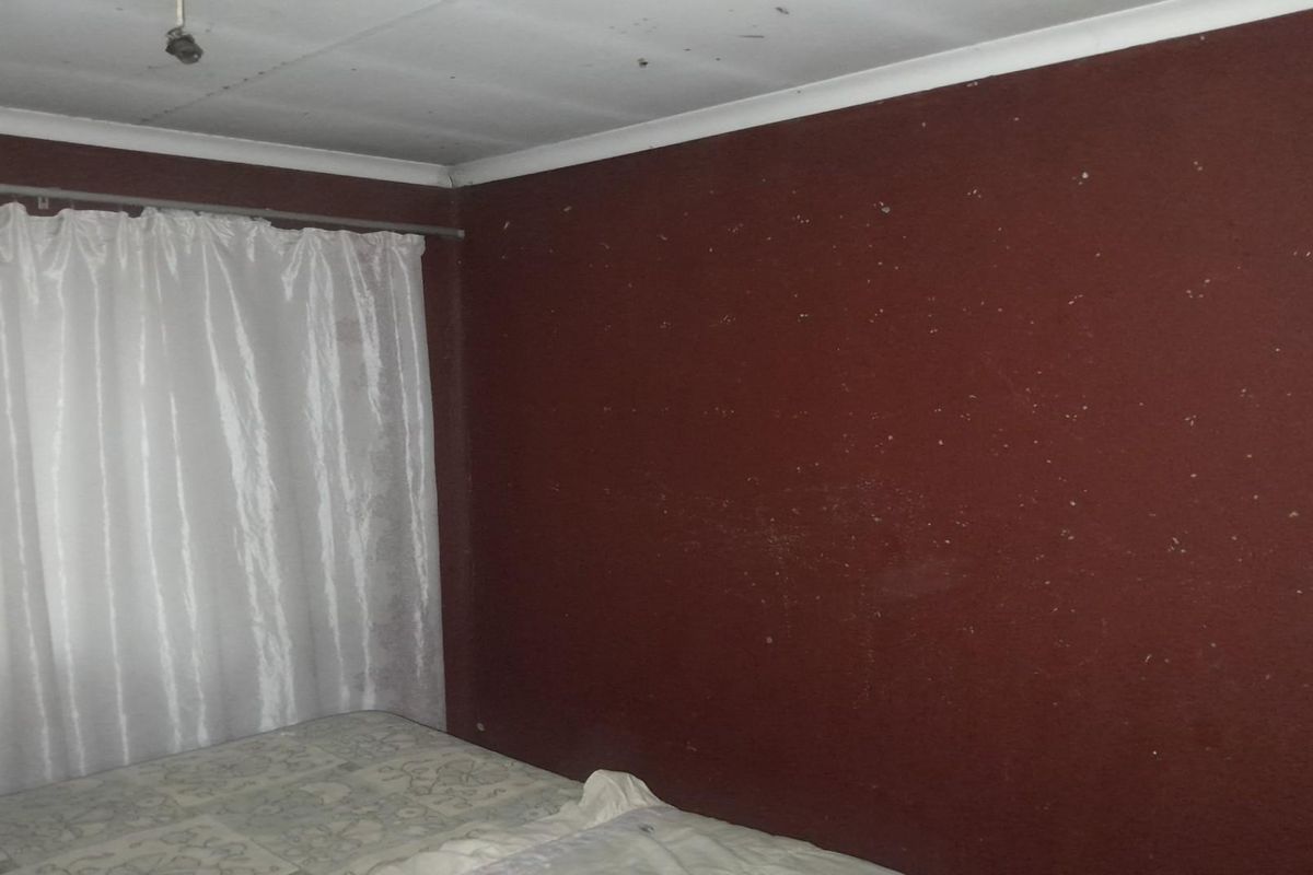 A bedroom featuring dark red painted walls and a white ceiling, showing signs of wear and surface damage.