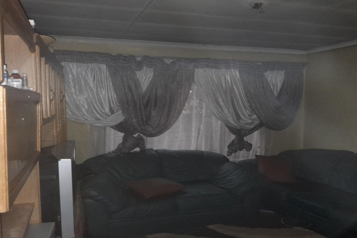 A dimly lit living room featuring a built-in wooden cabinet, large window with curtains, and a visible electrical distribution board.