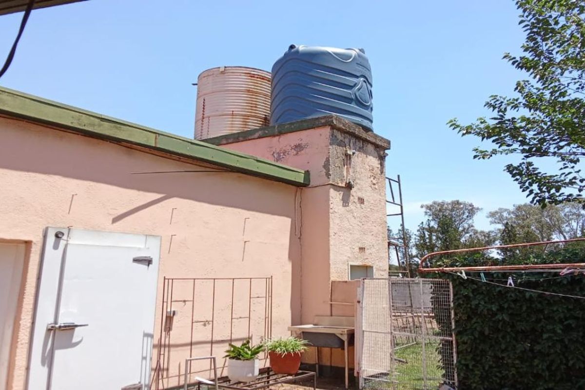 Exterior view of a farm building featuring two rooftop water storage tanks, a utility sink, and weathered exterior wall finishes.