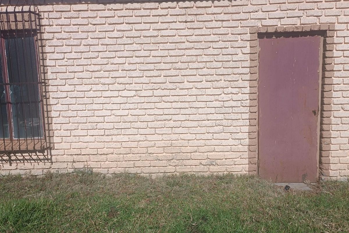 Exterior view of a farm building featuring a painted brick facade, a metal security door, and a window with protective iron bars.