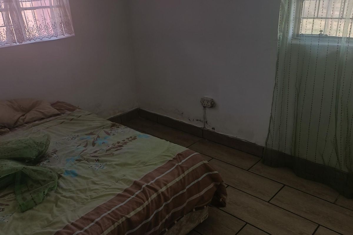 A bedroom featuring tiled flooring and dual windows, showing signs of wall moisture and surface wear requiring maintenance.