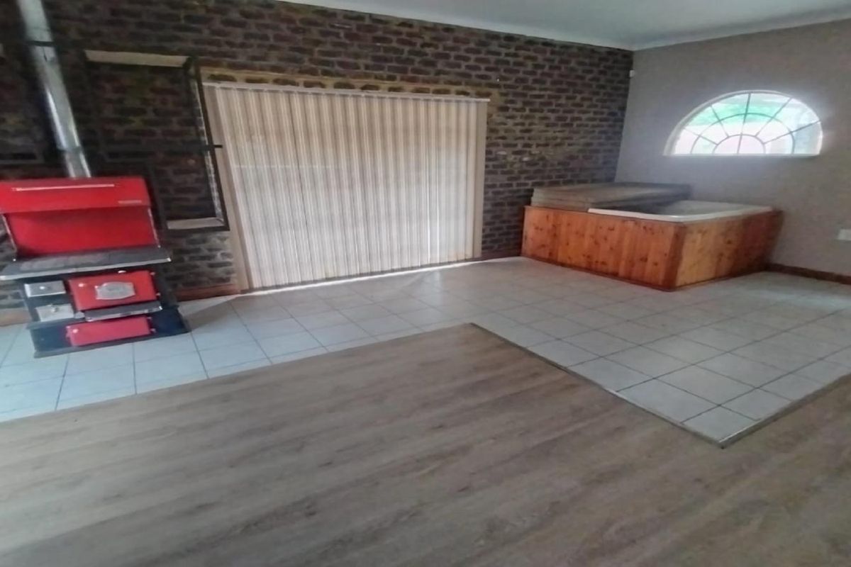 A living area featuring a brick feature wall, a built-in wood-burning stove, tiled and wood-look flooring, and a built-in wooden spa enclosure.