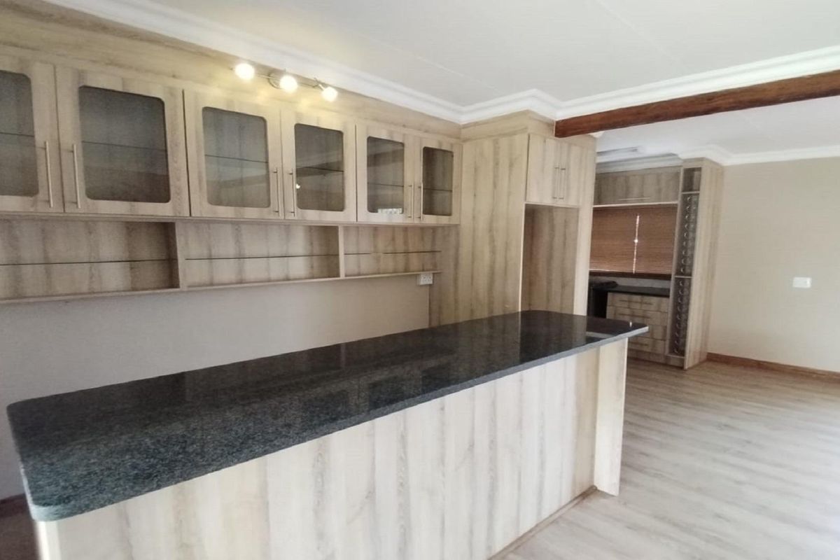 A modern kitchen area featuring light wood-grain cabinetry, a dark granite breakfast bar, and integrated shelving, offering a clean and functional layout.