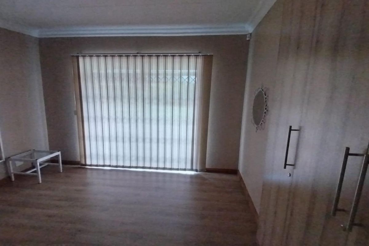 A bedroom featuring wood-look laminate flooring, built-in cupboards with modern handles, and vertical blinds covering the window.