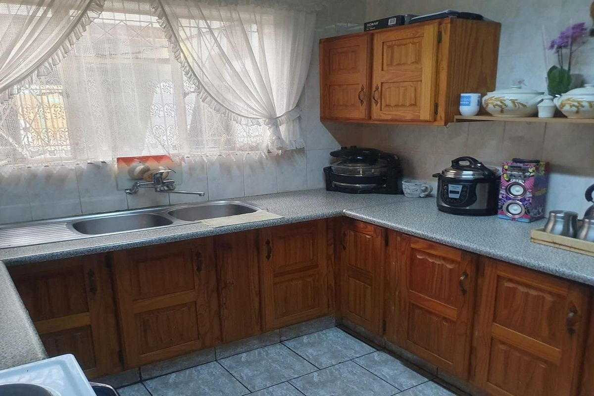 A functional kitchen featuring traditional wooden cabinetry, laminate countertops, a double-basin stainless steel sink, and tiled flooring.