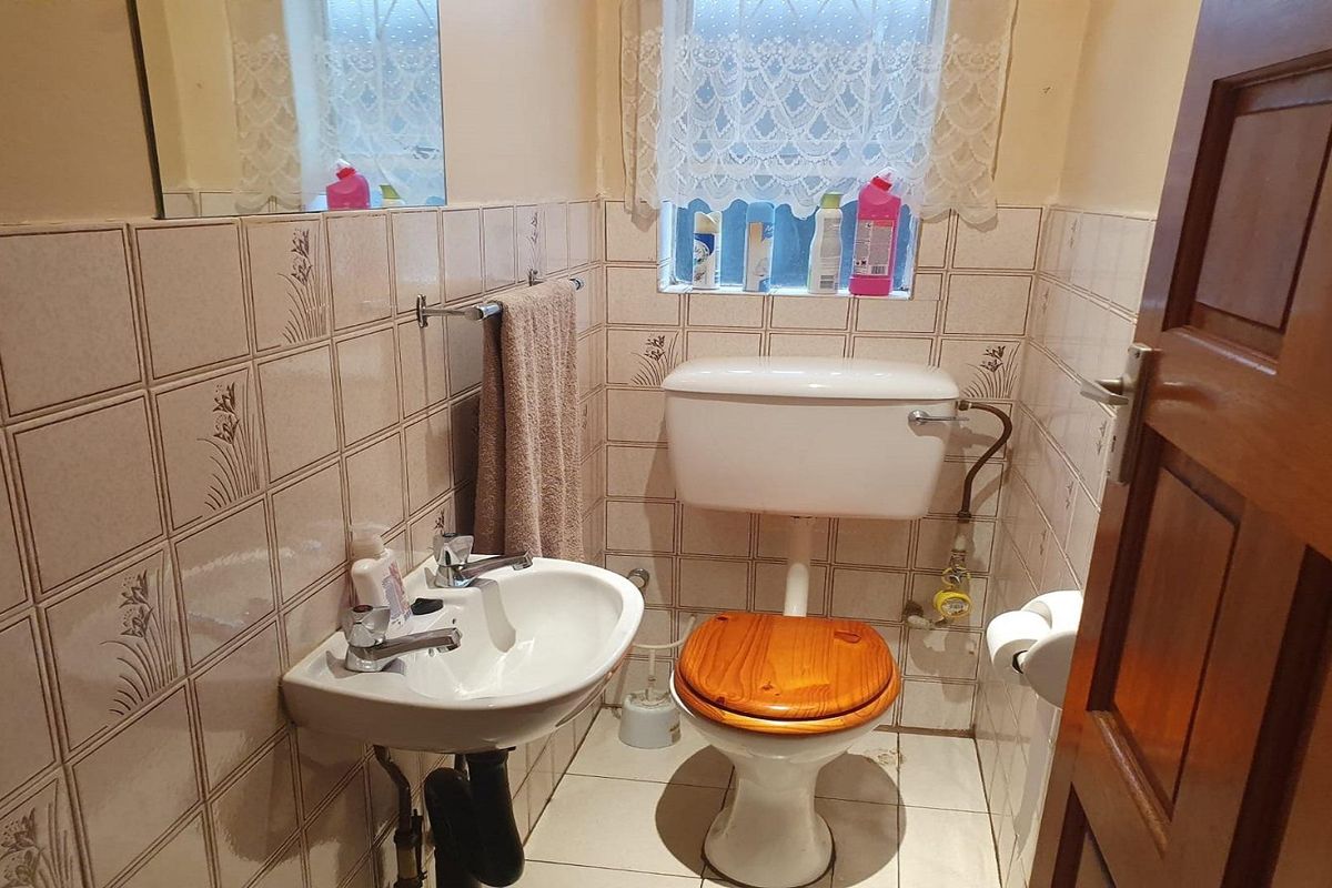 A compact bathroom featuring dated wall tiles, a pedestal sink, and a standard toilet, requiring modernization to improve functionality and aesthetic appeal.