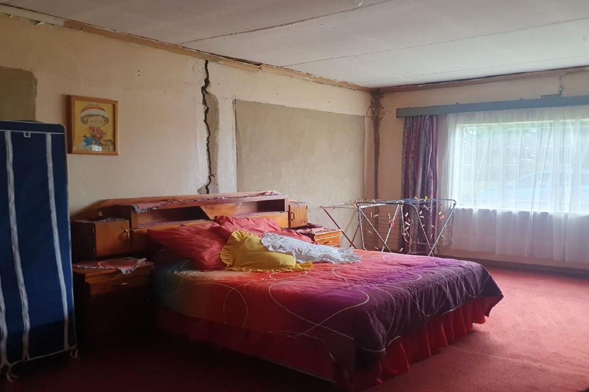 A bedroom featuring a large vertical crack in the wall and dated finishes, requiring significant repair and renovation.