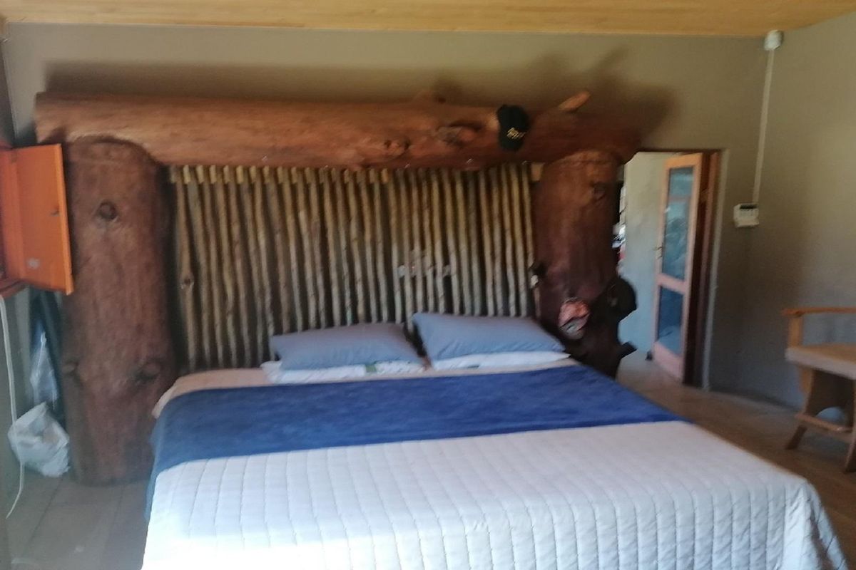 A rustic bedroom featuring a unique log-style headboard, timber ceiling, and direct access to an adjoining room.