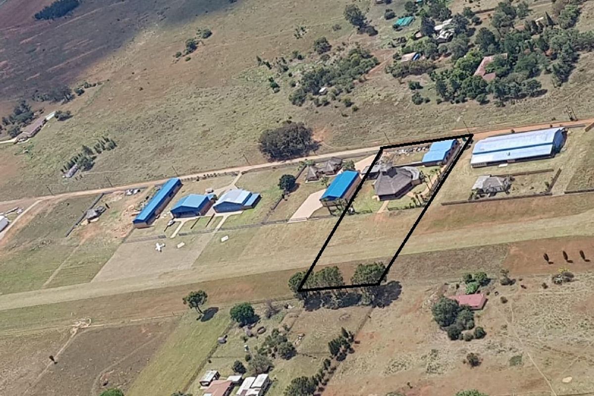 Aerial view of a rural property featuring a main residence, multiple outbuildings, and a private airstrip within a large fenced plot.