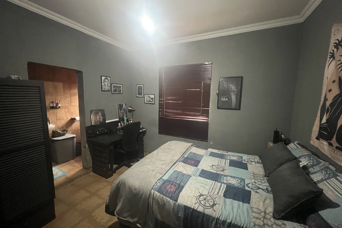 A bedroom featuring tiled flooring, a built-in en-suite bathroom, and window blinds, offering a functional living space.