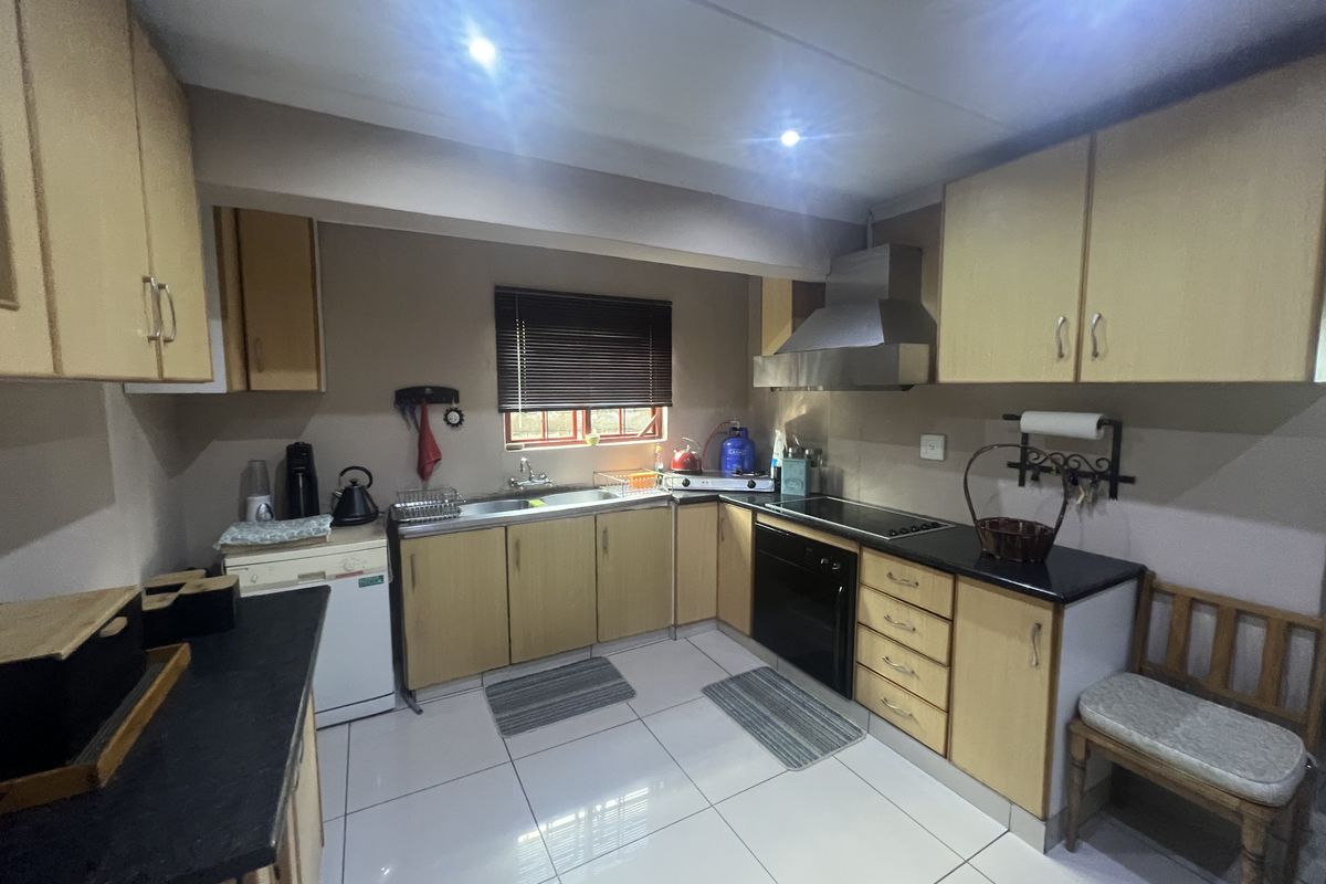 Functional kitchen featuring light wood cabinetry, black countertops, built-in oven, extractor fan, and tiled flooring with recessed ceiling lighting.