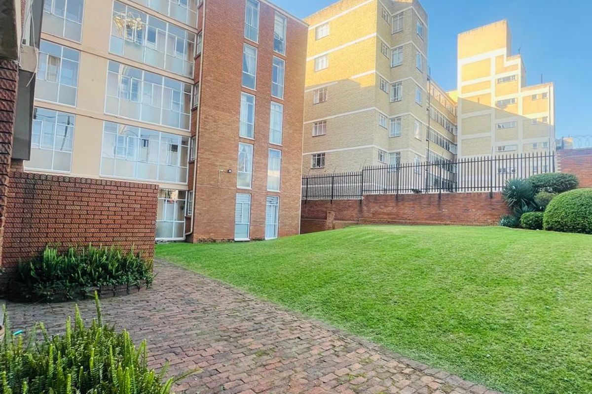 A view of the apartment complex exterior featuring a communal lawn, brick paved pathways, and established garden beds.