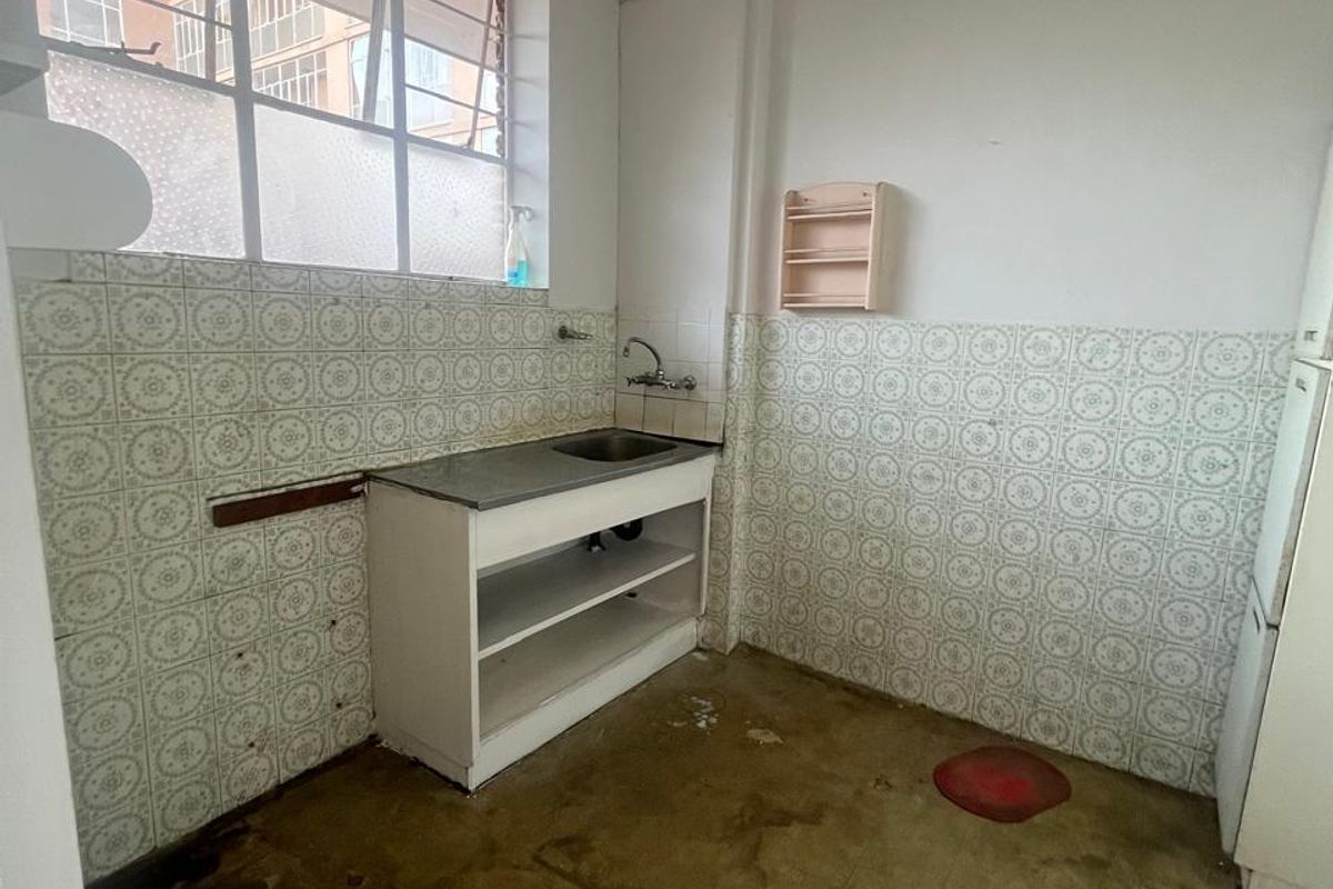 A dated kitchen area featuring original wall tiling, a basic sink unit, and worn flooring, offering significant potential for renovation and modernization.