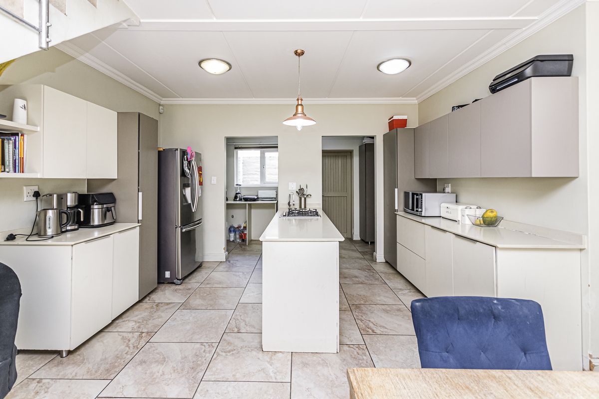 Modern kitchen featuring a central island with gas hob, ample built-in cabinetry, stone countertops, and tiled flooring, with an adjacent scullery area.