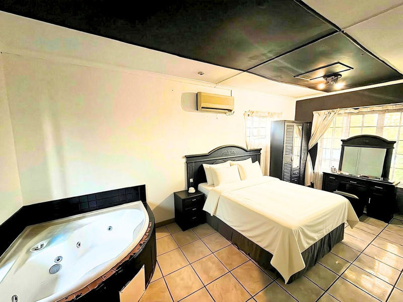 A bedroom featuring an integrated corner bathtub, tiled flooring, and a split-system air conditioner, with a unique dark-toned ceiling design.