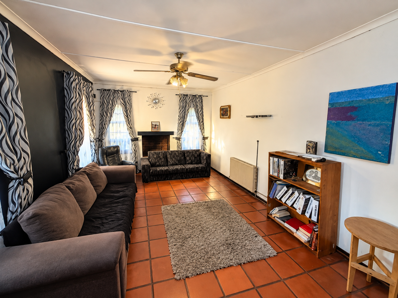 A living room featuring terracotta floor tiles, a brick fireplace, a ceiling fan, and a wall-mounted radiator.
