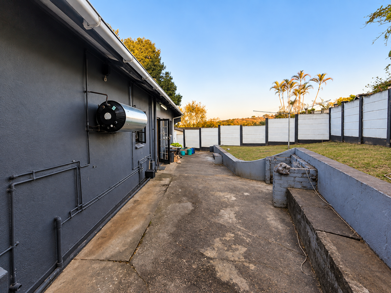 Rear exterior area featuring a concrete patio, built-in brick braai, perimeter walling, and an externally mounted electric geyser.