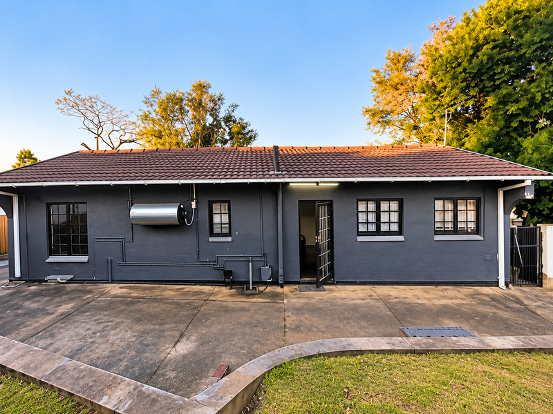Rear exterior view of the house featuring a dark painted facade, tiled roof, external geyser, and a concrete patio area.