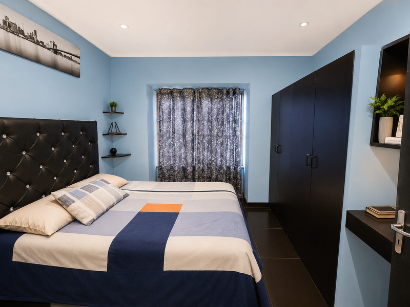 A well-maintained bedroom featuring built-in black cabinetry, recessed downlighting, and floating shelving, finished with light blue walls and dark floor tiles.