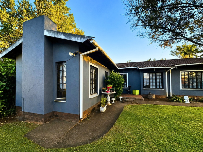 Rear view of a single-story house featuring a prominent brick chimney, dark blue exterior walls, tiled roofing, and a surrounding garden with concrete pathways.