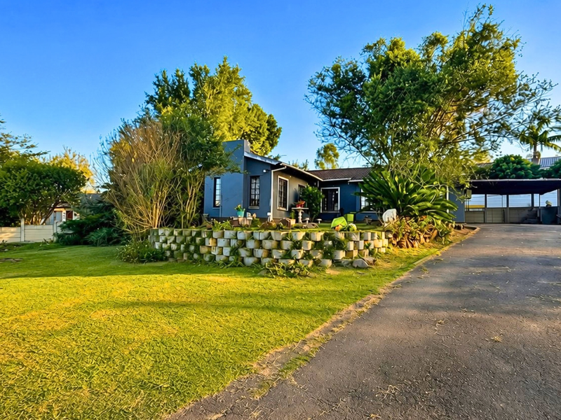 Front exterior view of a single-story house featuring a retaining wall, landscaped garden, and an adjacent carport with a paved driveway.
